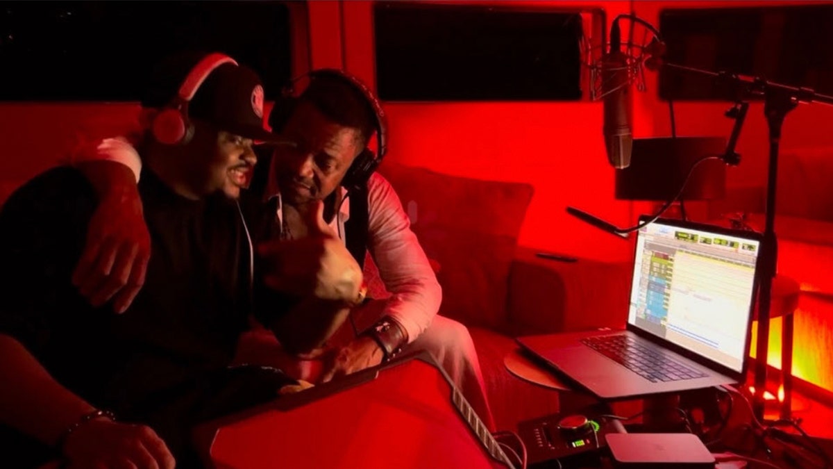 Rodney Jones sitting in a recording studio in dim lighting as another man sits beside him with an arm on his shoulder