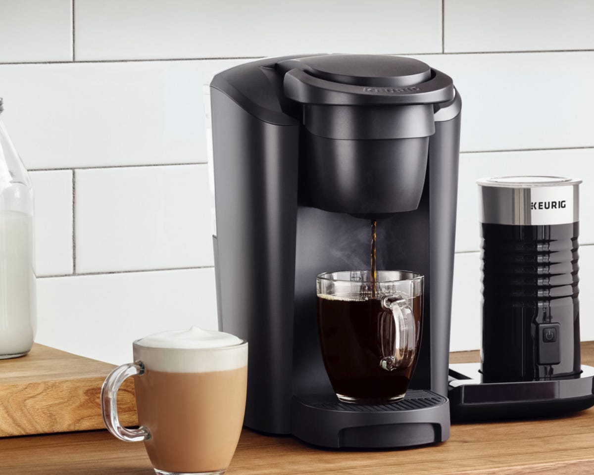 Photo of a black Keurig K latte machine with latte and milk frother on table with white tile background