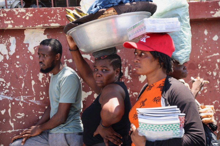 People on the streets of Port-au-Prince. One woman has a large metal container n her head filled with belongings. Another is balacing two books on her head and carryying more in her arm