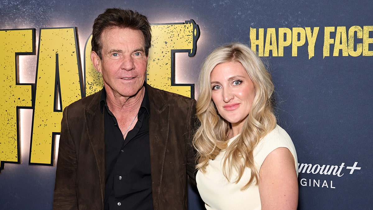 Melissa G. Moore in a creme dress posing next to Dennis Quaid wearing a dark shirt and a brown jacket.