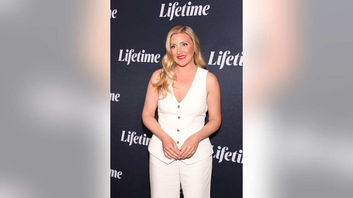 Melissa G. Moore wearing a white top and matching pants smiling for cameras.