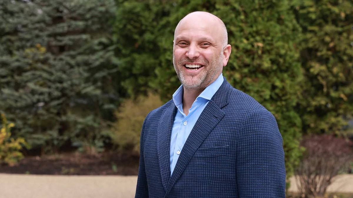 Jason Friedman smiling in a blue blazer outdoors in front of greenery