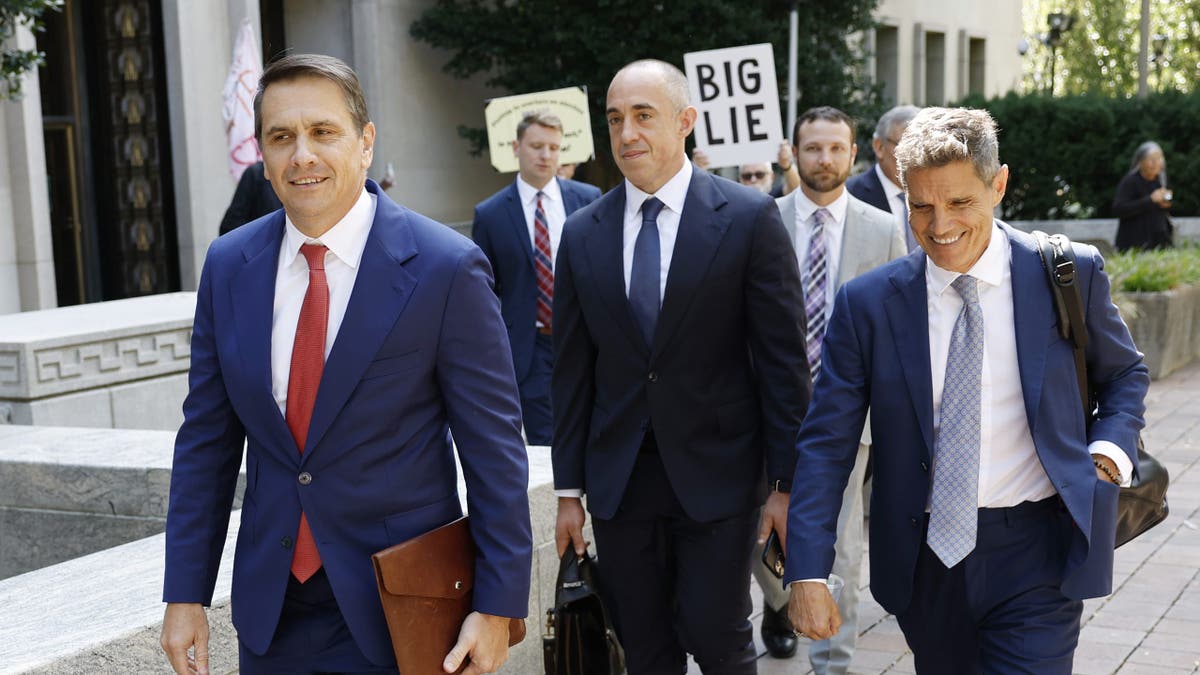 Emil Bove, center, walks with members of former President Trump’s legal team outside federal court in Washington, D.C., with a protester holding a "BIG LIE" sign in the background.