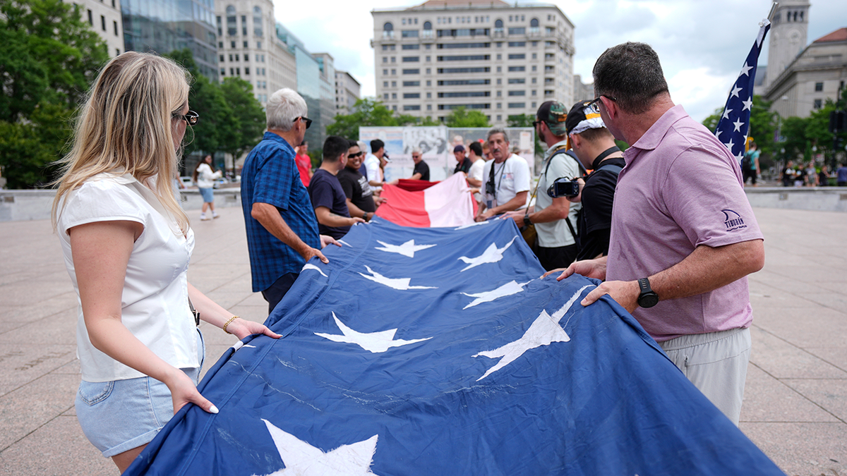 People fold a large American flag at Freedom Plaza before a parade commemorating the Army's 250th anniversary on Saturday, June 14, 2025, in Washington.
