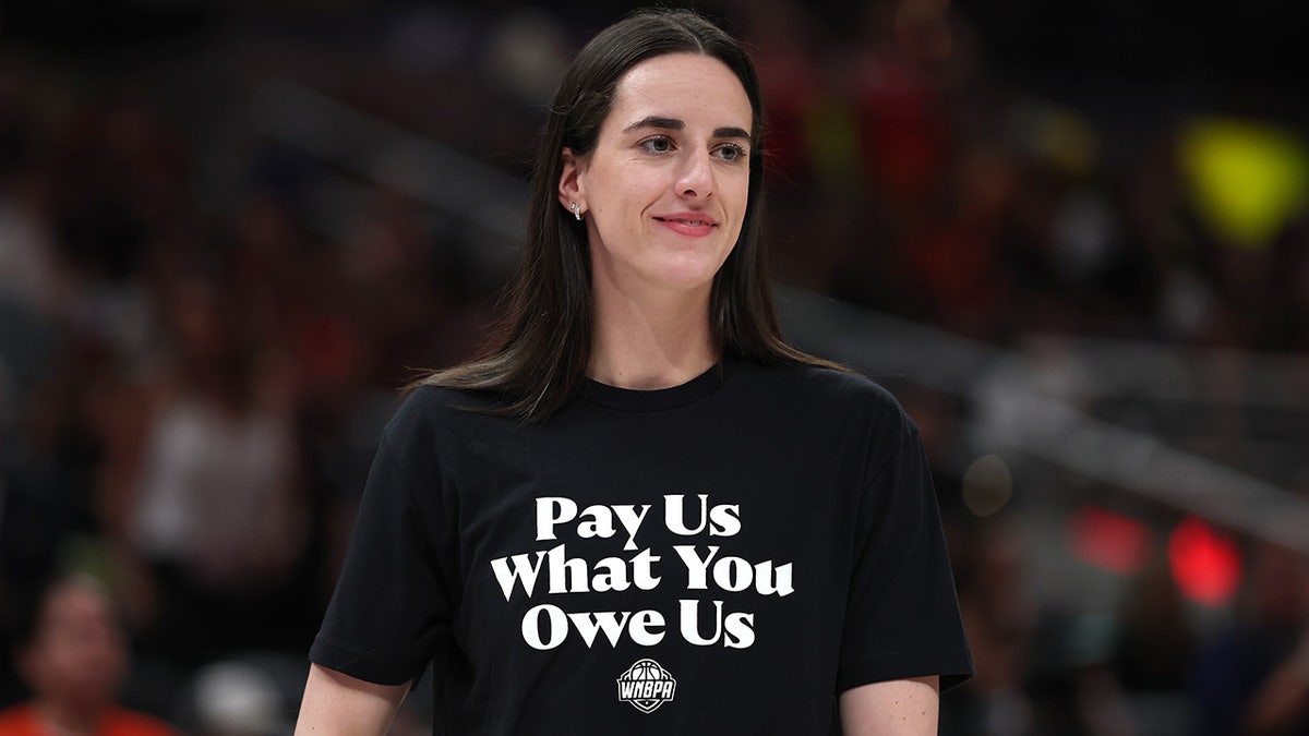 Caitlin Clark wears a black shirt that says "Pay us what you owe us"