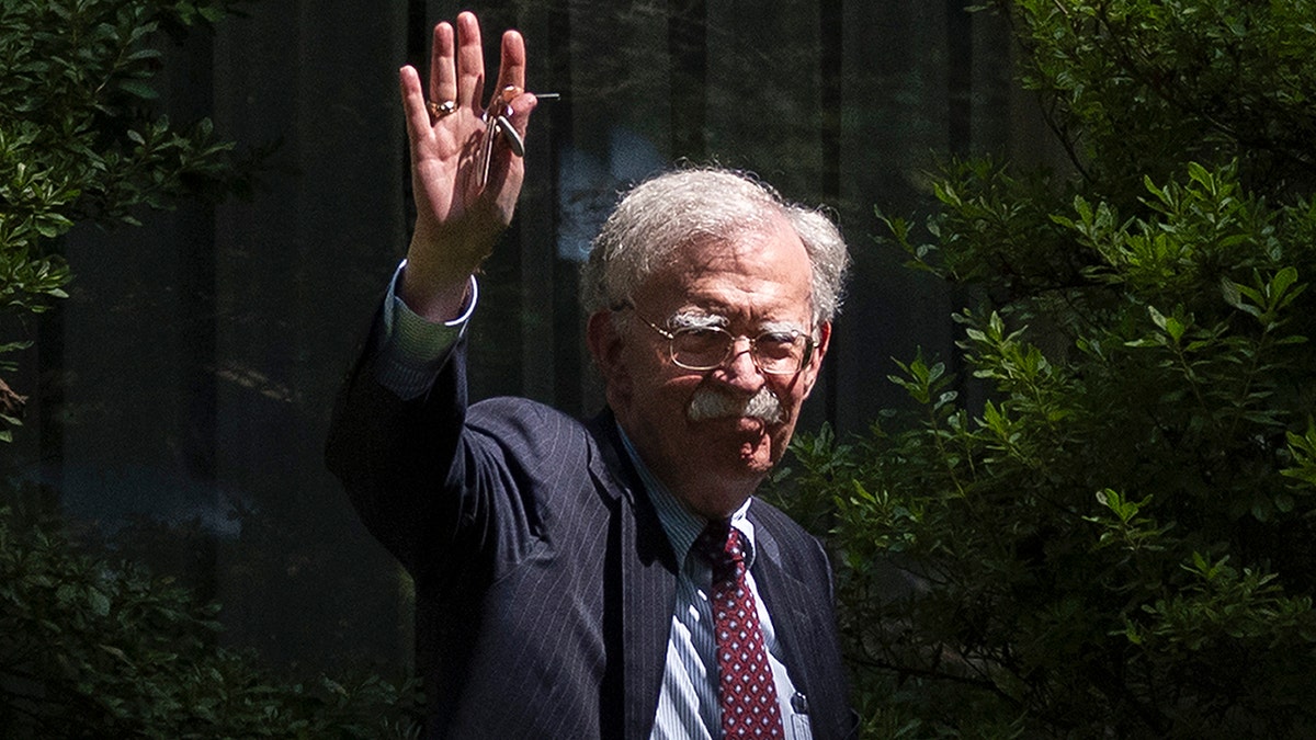 John Bolton in suit waving outside his home