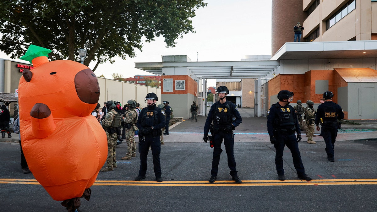 A protester in a giant orange costume stand outside an ICE facility.