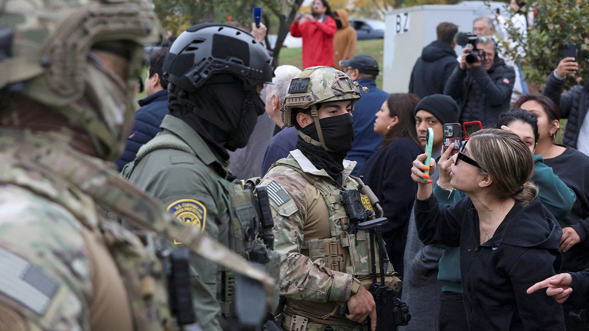 Woman holds her phone up while interacting with federal agents in Chicago.
