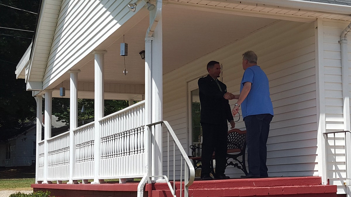 A pastor and a man shake hands outside on the porch of the church.