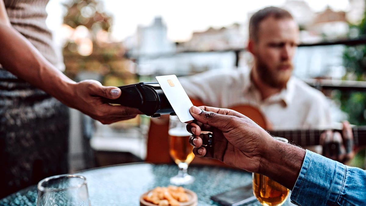 Hand reaching out across table to pay for meal outdoors with a credit card - contactless payment