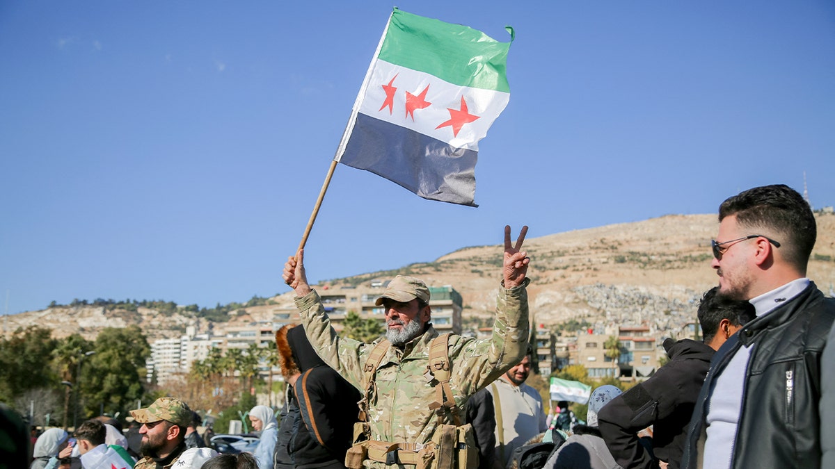 A man raises the Syrian opposition flag amid a crowd in Damascus.