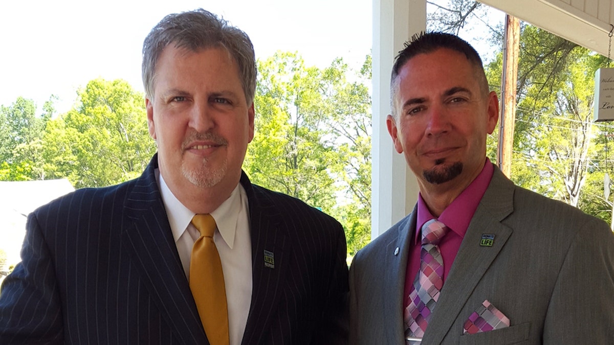 Two men standing outside smiling at the camera.