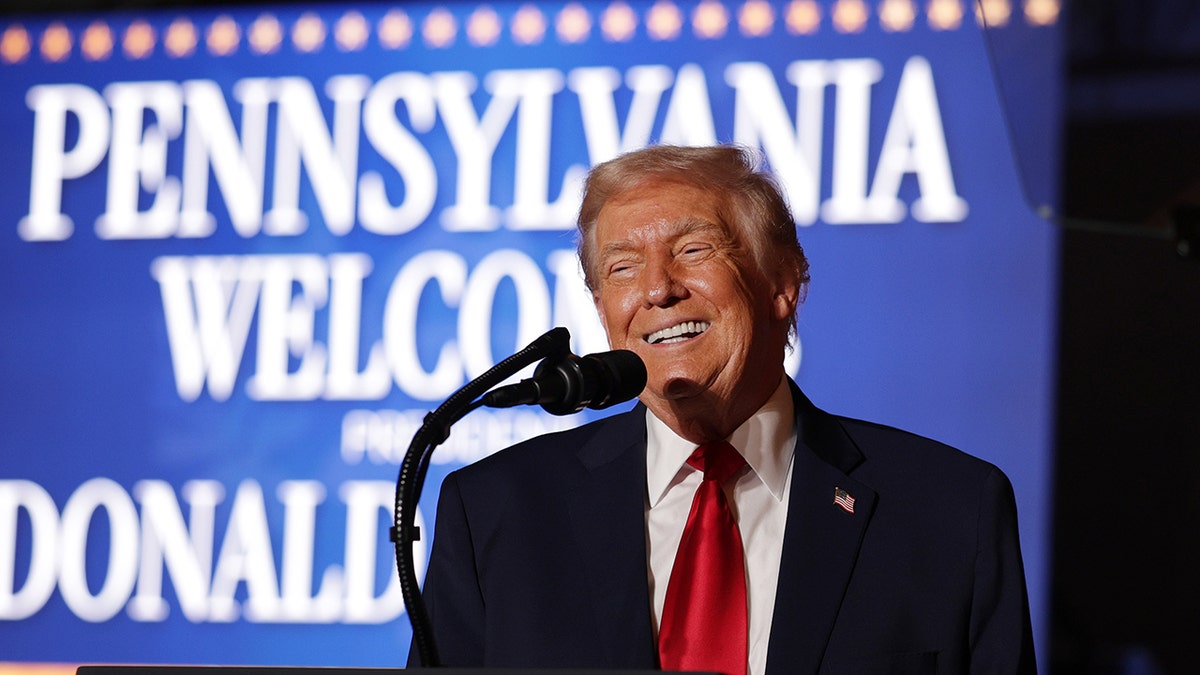 President Donald Trump smiles while speaking at podium.