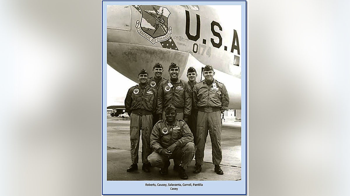 Servicemembers pose in flight suits in front of a B-52 bomber on a military airfield.