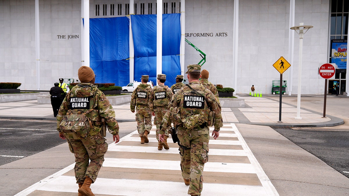National Guard soldiers walk across a crosswalk toward the Kennedy Center as exterior signage work continues.