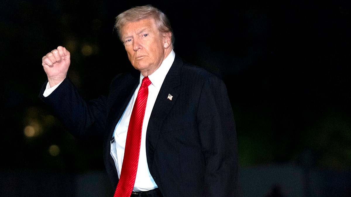 President Donald Trump wearing a dark suit and red tie as he walks with his arm raised in a gesture.