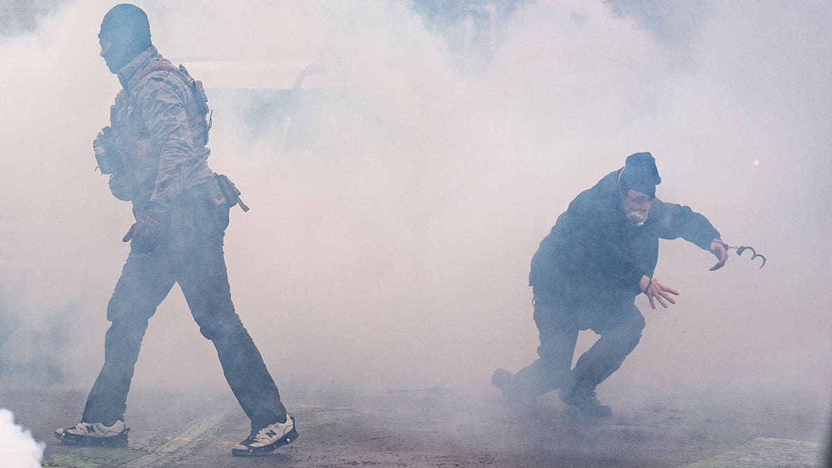 A man wearing handcuffs running through a cloud of tear gas.