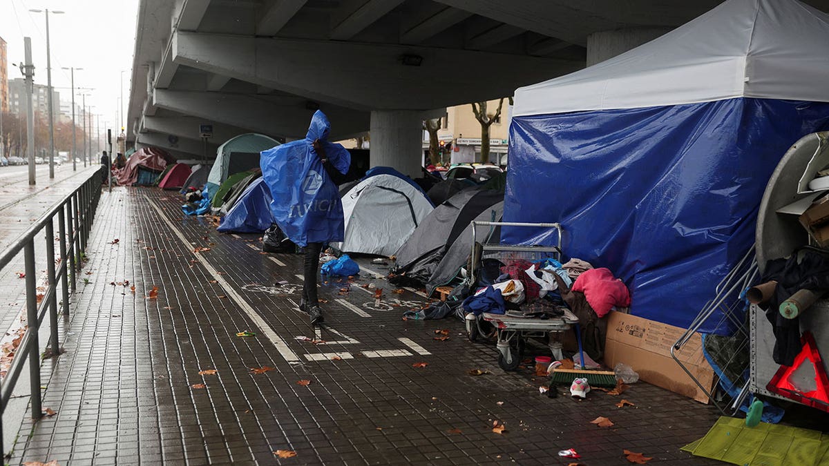 A migrant walks by a makeshift settlement where migrants evicted from a former high school last week are camping outdoors in the middle of winter in Badalona, Spain