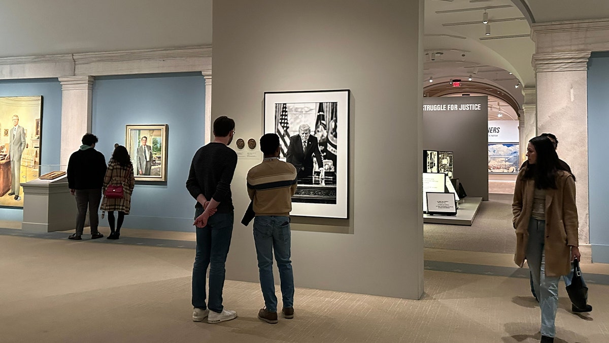 two visitors look at a presidential portrait of trump at a museum