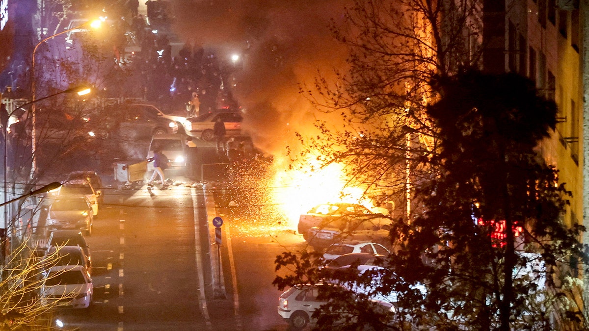 Burning cars line a street in Tehran as thick smoke rises during unrest.