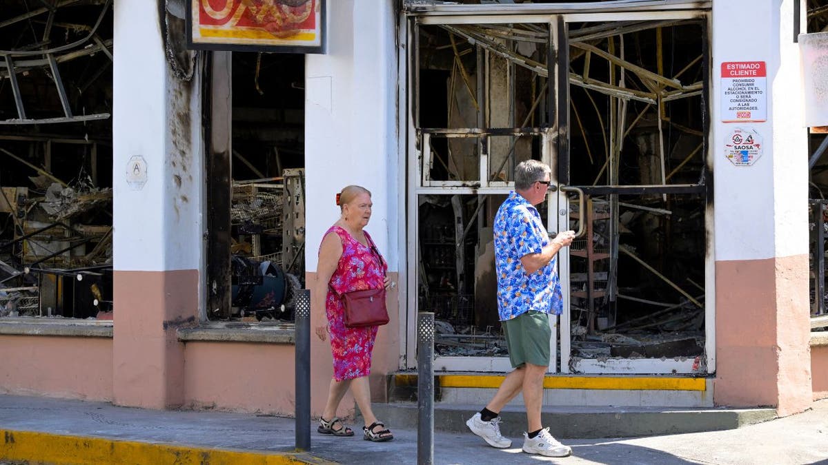 Tourists walk past a burned storefront in Puerto Vallarta after cartel violence in Jalisco, Mexico.