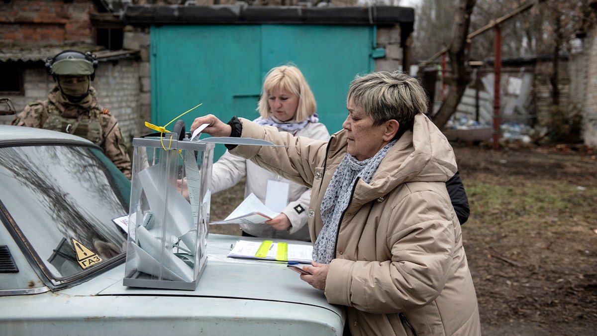 A voter places her ballot into a portable ballot box inside a temporary polling setup in a conflict-affected area.