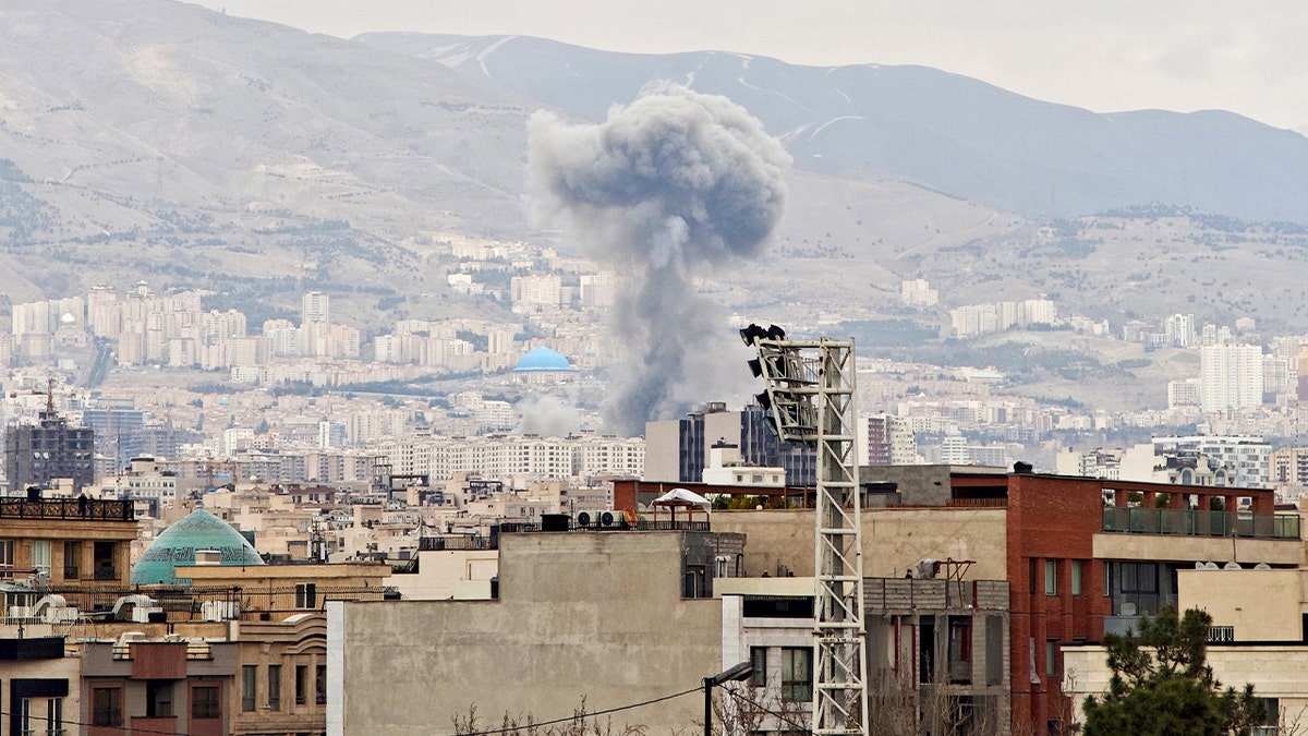 A tall column of smoke billows into the sky over Tehran after a significant explosion.