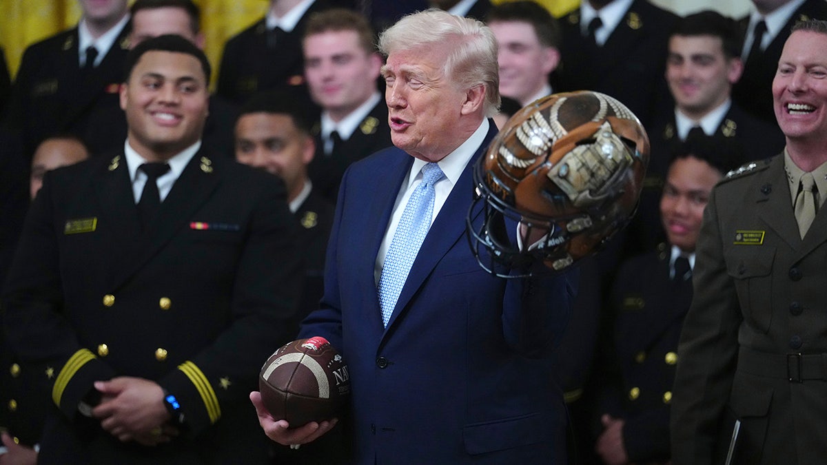 Trump holds up a helmet as he speaks during the Commander-in-Chief's Trophy presentation