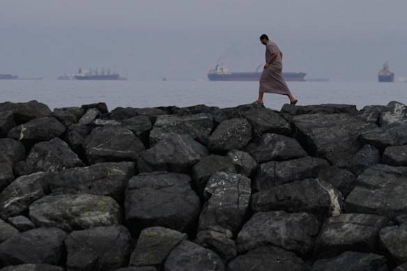 A man walks along the shore as oil tankers and cargo ships line up in the Strait of Hormuz.