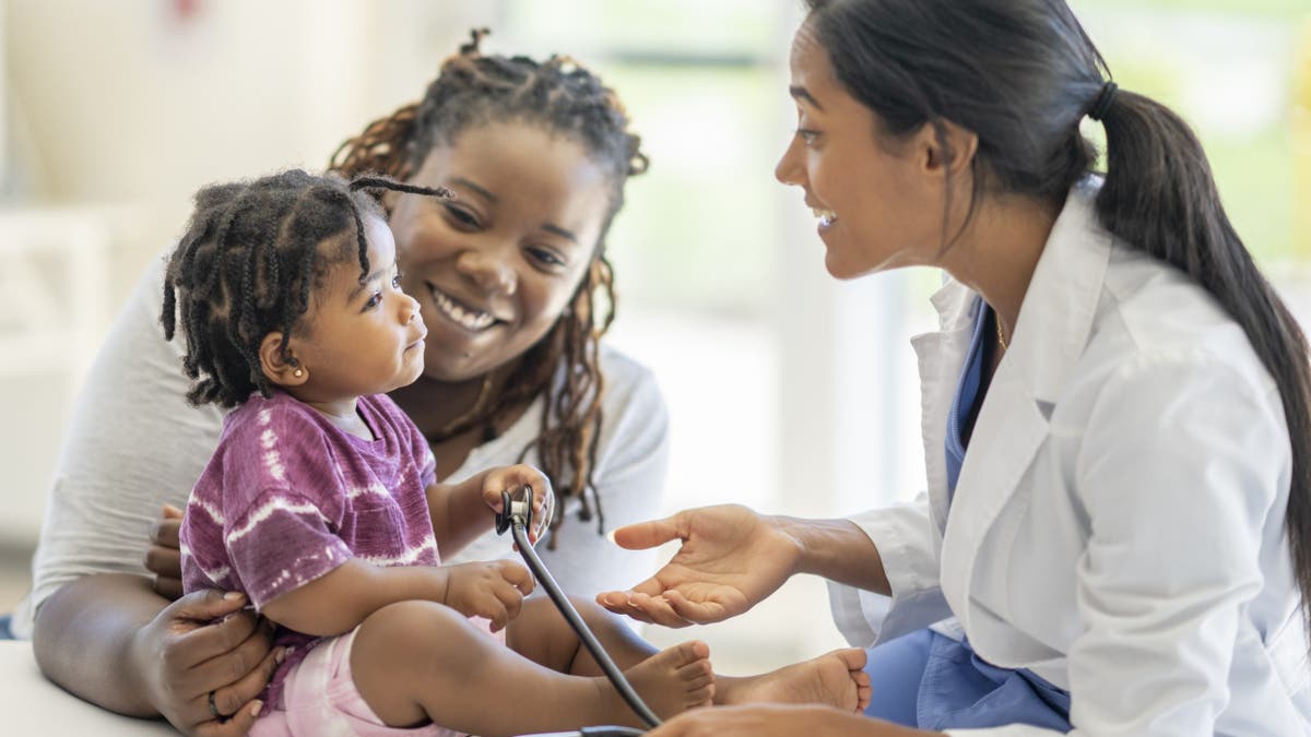 A female doctor in a white lab coat sitting with a mother and her young son in a medical clinic.