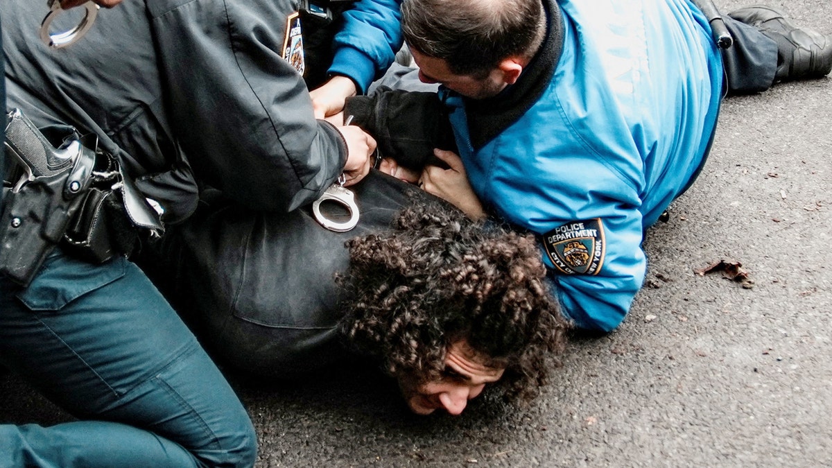 A man on the ground with NYPD officers on top of him