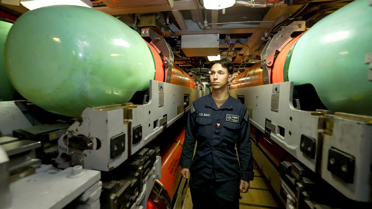 A U.S. service member examines a large torpedo mounted inside a submarine’s weapons compartment while the vessel is moored in Australia.