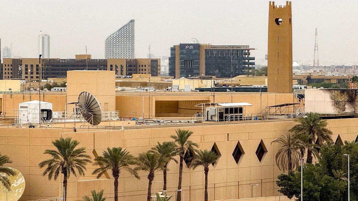 The U.S. Embassy compound in Riyadh shows visible damage after reported drone strikes, with the surrounding city skyline in view.