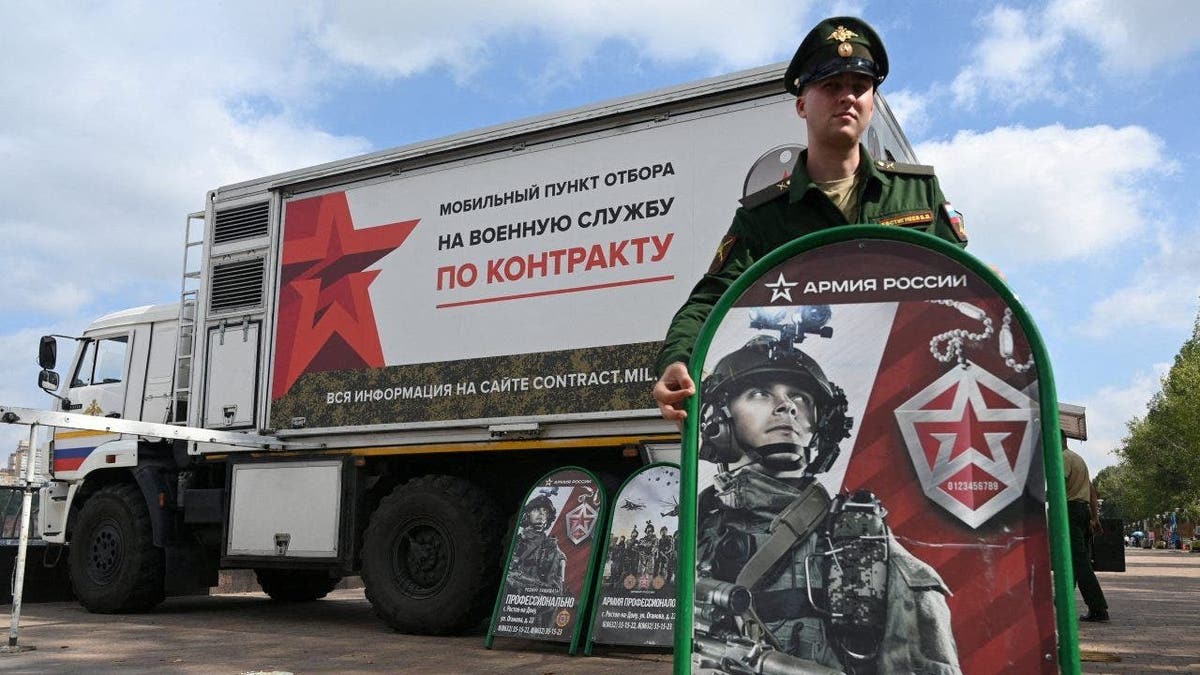 A Russian service member standing next to a mobile recruitment center in Rostov-on-Don