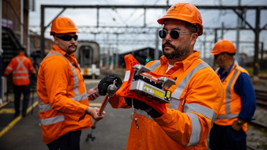 Workers demonstrate a new hand-held laser device used to check over-head wiring on Sydney’s passenger train network.