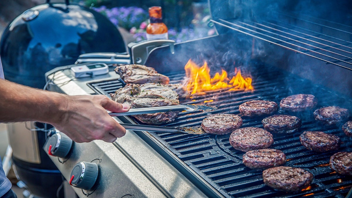 Lamb joint and beef burgers cooking on a barbecue grill.