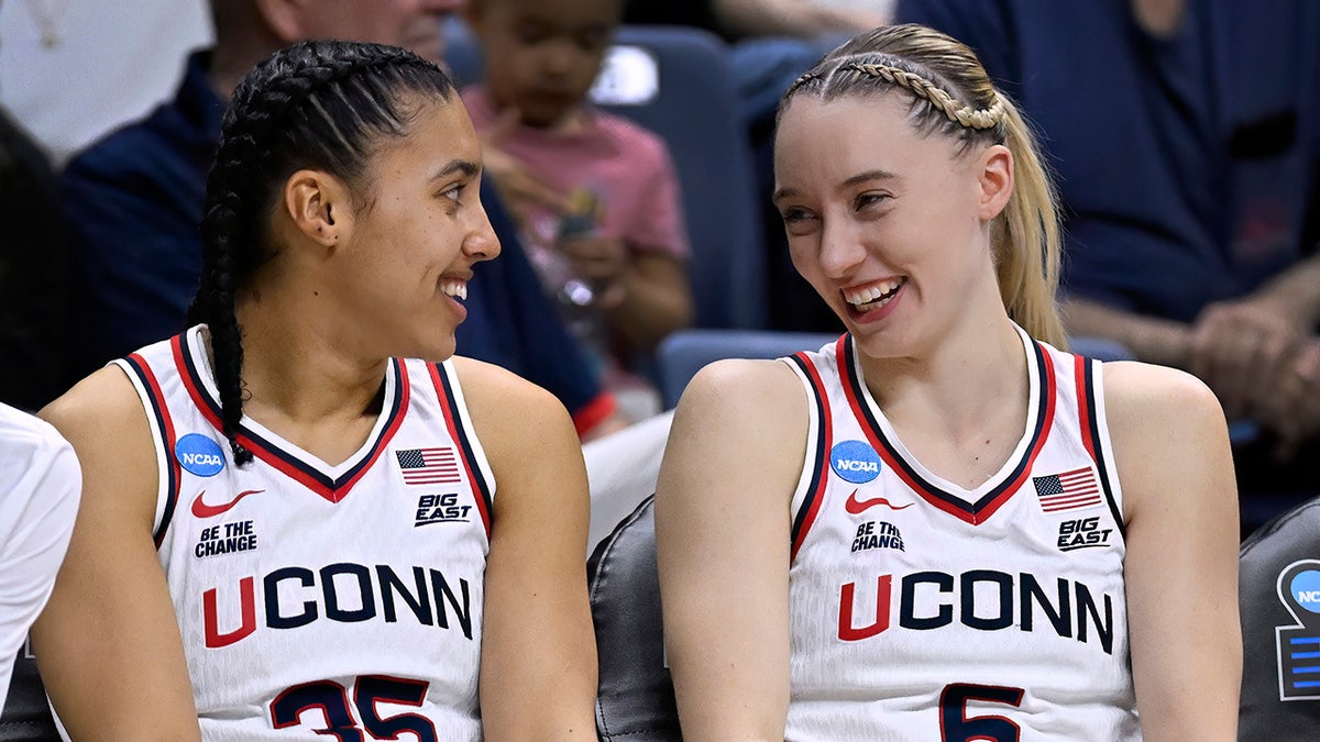 UConn guards Azzi Fudd and Paige Bueckers smiling at each other on the bench