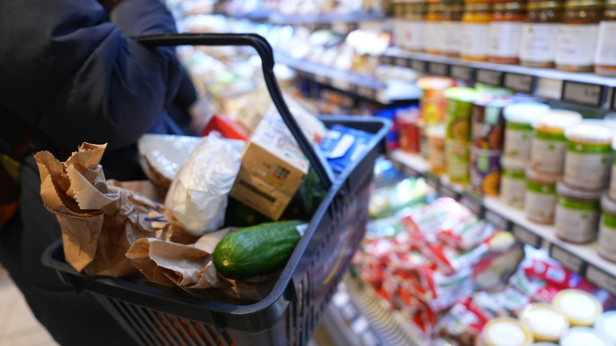 A customer walks past the shelves in a supermarket with a shopping basket.