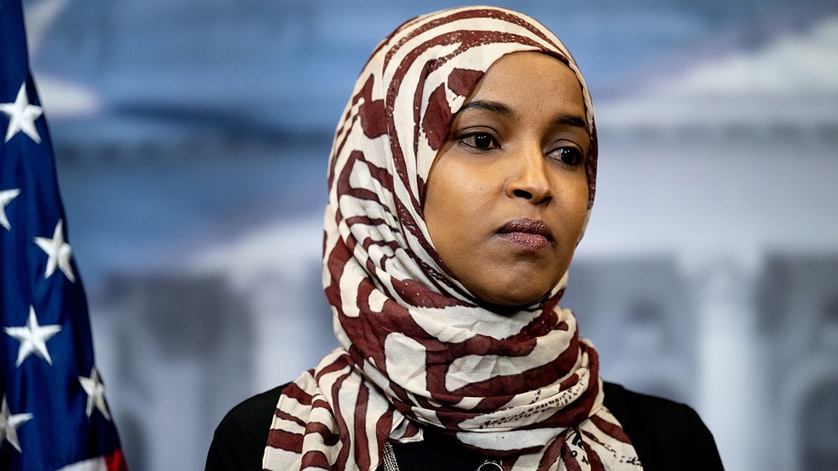 Rep. Ilhan Omar standing with a serious expression during a news conference at the U.S. Capitol in Washington, D.C.