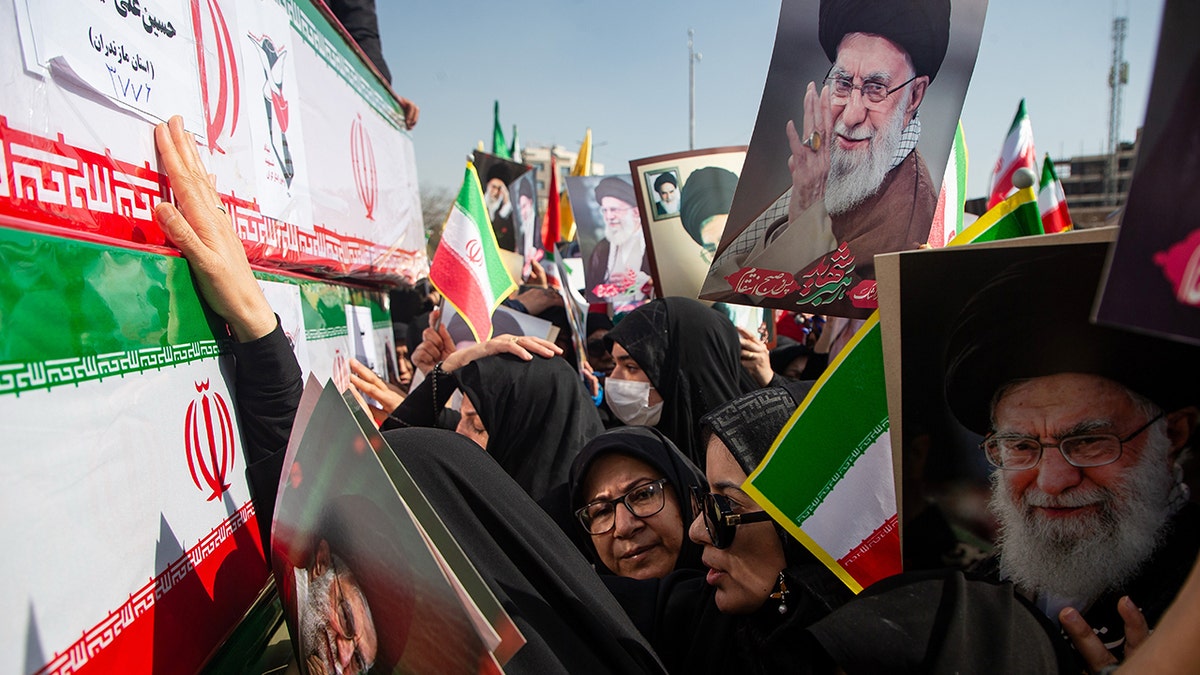 Mourners reaching out to touch coffins while holding pictures of Ayatollah Ali Khamenei during a funeral in Isfahan.