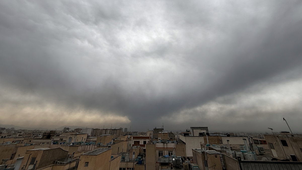Plumes of dark smoke rising from an oil facility in Tehran, Iran, merging with a cloudy sky.