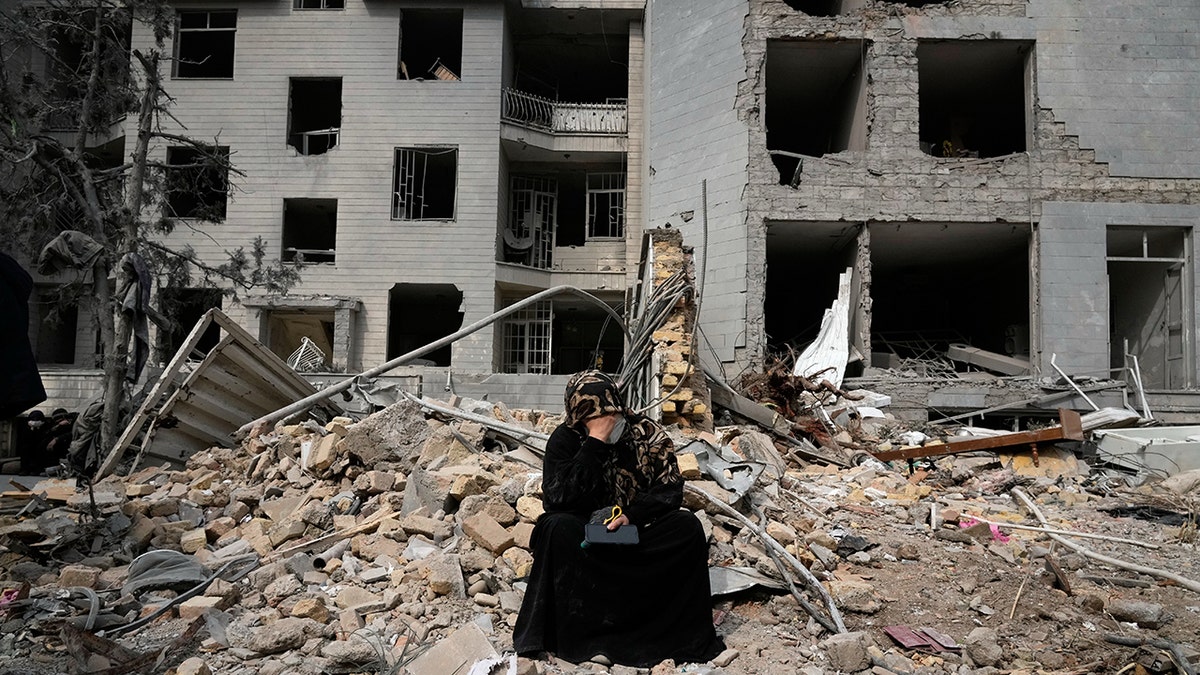 A woman sitting on rubble in front of a building in Tehran.