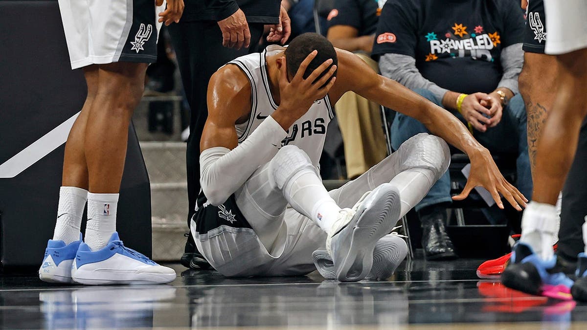 Victor Wembanyama holding his head after falling on the basketball court