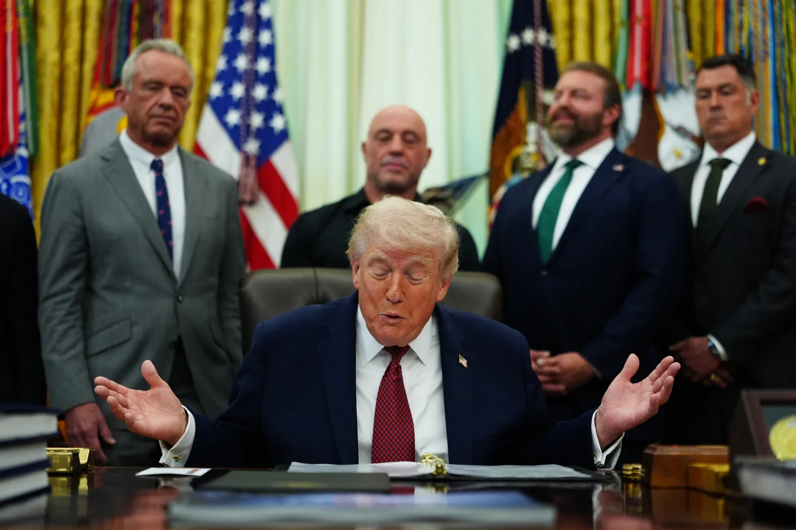 President Donald Trump speaks while behind him, from left, Health and Human Services Secretary Robert F. Kennedy Jr., podcaster Joe Rogan, Americans for Ibogaine CEO W. Bryan Hubbard and retired Navy SEAL Marcus Luttrell listen in the Oval Office of the White House, on April 18 in Washington, D.C. (AP Photo/Julia Demaree Nikhinson)