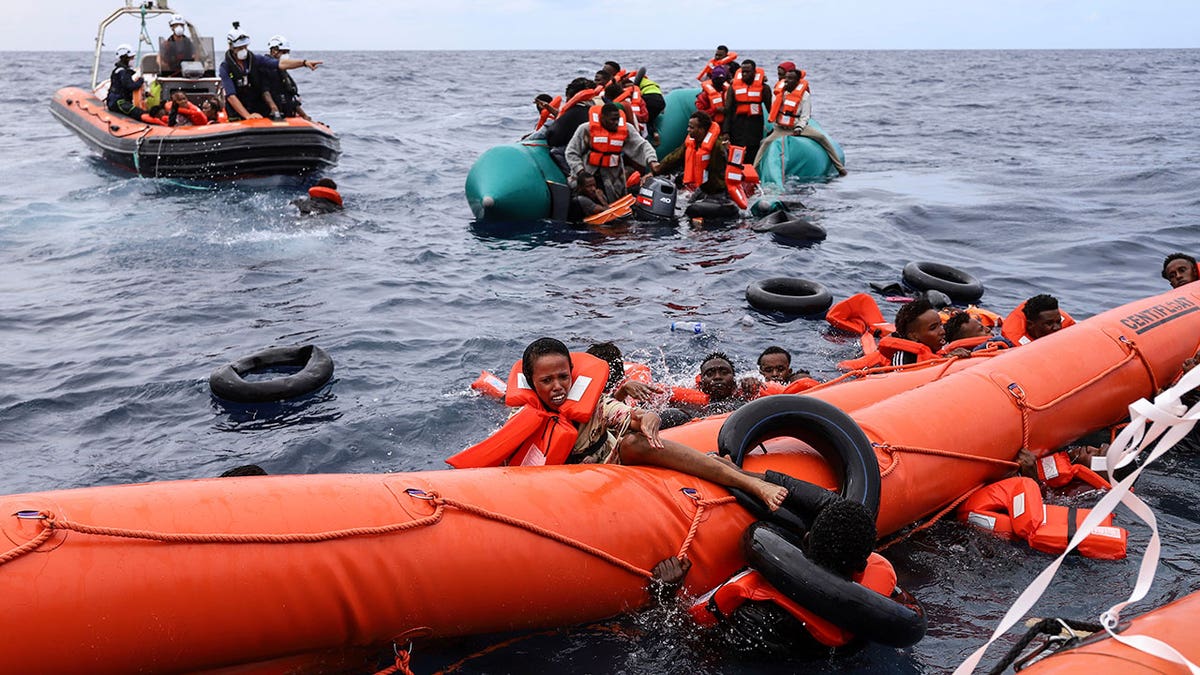 Migrants aboard a rubber boat falling into water near a rescue boat