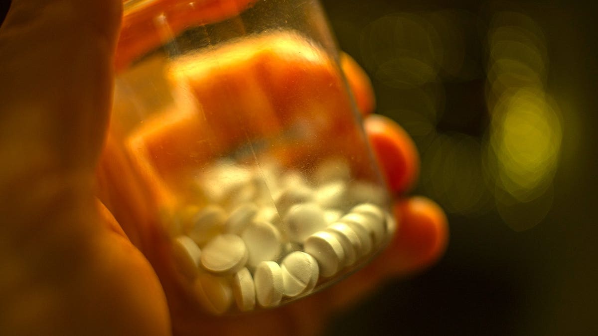 A man's hand holding a plastic bottle with white antidepressant pills