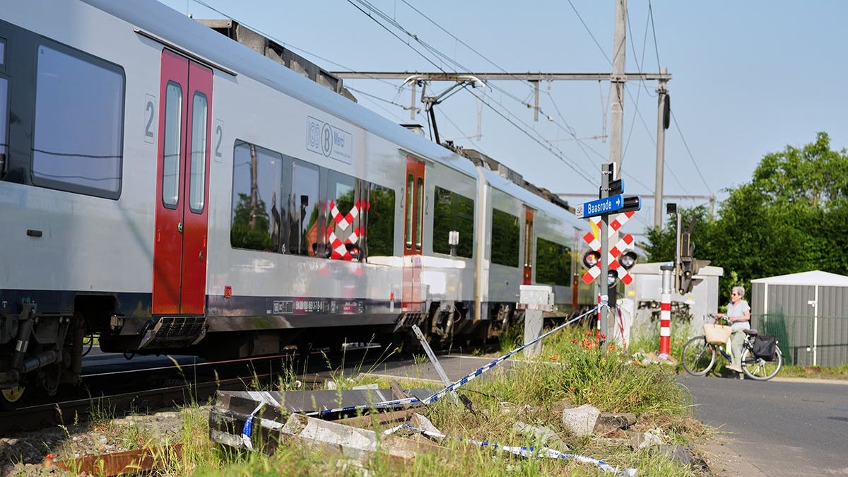 A woman on a bike standing next to police tape and debris at a level crossing
