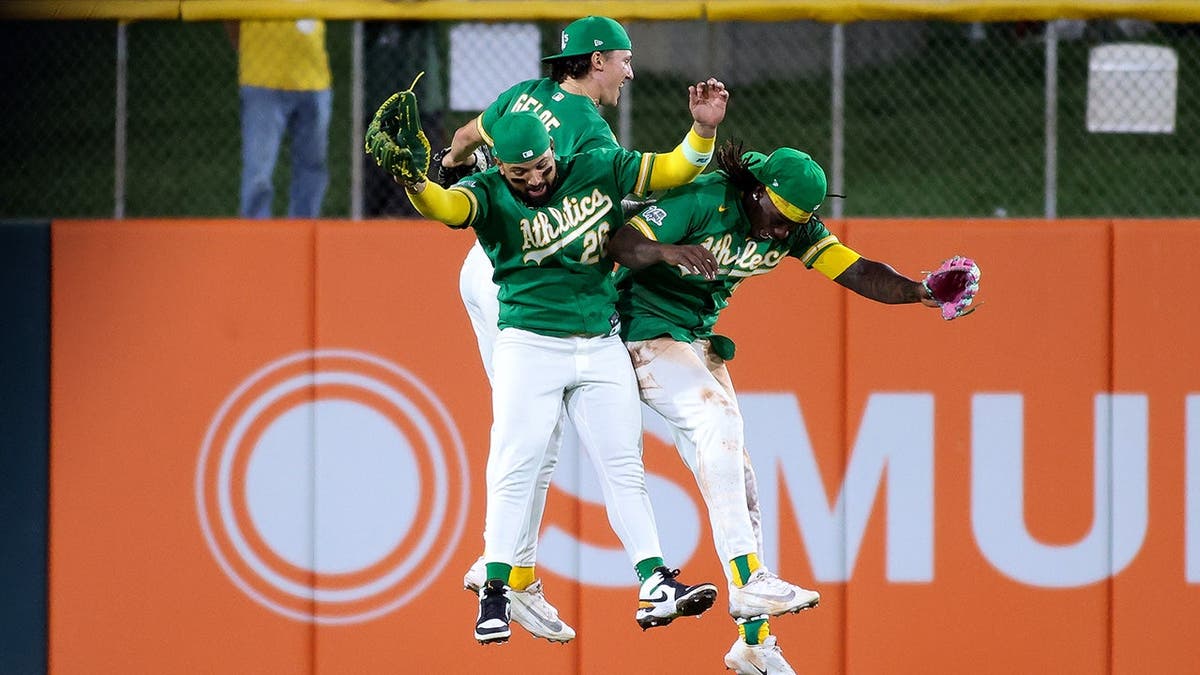 Athletics left fielder Carlos Cortes celebrating with teammates Zack Gelof and Lawrence Butler on baseball field