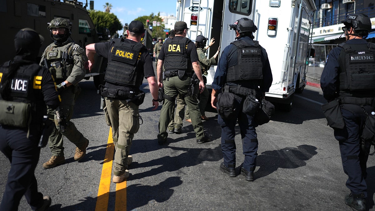 DEA agents and police officers standing near a white command vehicle on a Los Angeles street