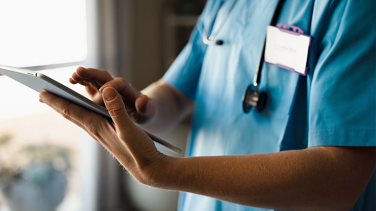 Female doctor in scrubs typing on a digital tablet